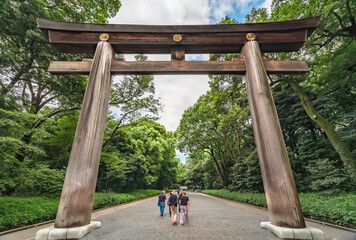 Tourists passing trough the wooden Ootorii sacred gate adorned with golden imperial coat of arms depicting chrysanthemum flowers in the Shinto shrine of Meiji-Jingu.