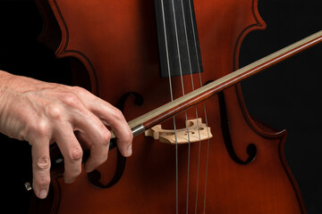 CLOSE UP OF MALE HAND PLAYING CELLO ON DARK BACKGROUND.