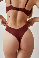 Closeup shot of back and buttocks of fit young caucasian woman in burgundy underwear adjusting her...