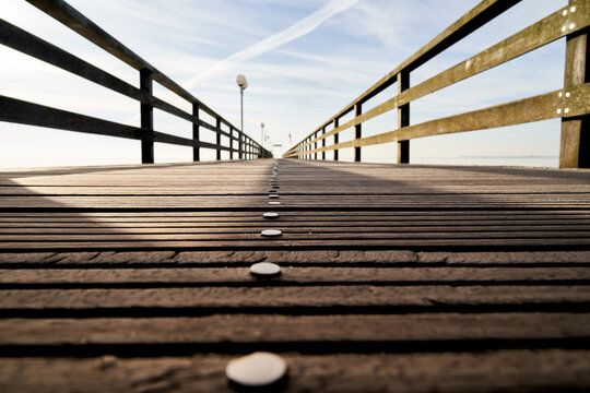 Ground view over an empty wooden pier with nails and a railing, central perspective with decreasing depth of field