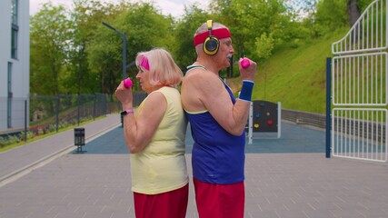 Active elderly sports team weightlifting dumbbells, smiling at camera. Outdoors portrait of...