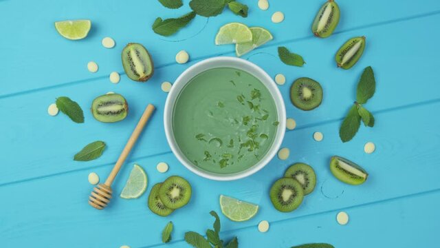 Sweet dessert with spirulina on a blue wooden background. with slices of kiwi, lime sprinkled with mint leaves