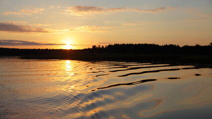 A beautiful orange sunset on the Volga River with a Sun in the sky and a forest on the horizon in the calm water on a summer evening