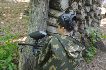A boy in protective clothing with a paintball gun in his hands.