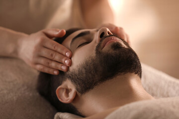 Fototapeta na wymiar Young man receiving facial massage in beauty salon, closeup