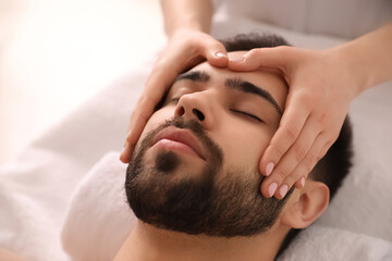 Fototapeta na wymiar Young man receiving facial massage in beauty salon, closeup
