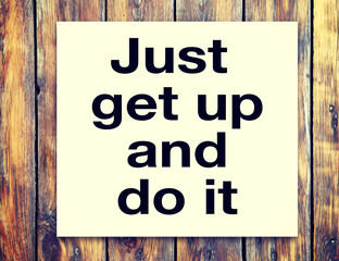 Motivational inscription on the sheet - Just get up and do it - against the background of a wooden table.
