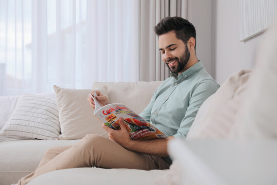Young man reading culinary magazine on sofa at home