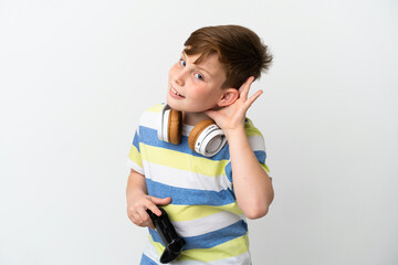 Little redhead boy holding a game pad isolated on white background listening to something by putting hand on the ear