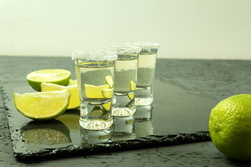 Three glasses with tequila and lime on a stone board