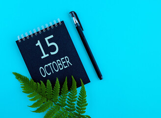 october 15th. Day 15 of month, Calendar date. Black notepad sheet, pen, fern twig, on a blue background. Autumn month, day of the year concept