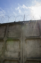 high concrete fence with barbed wire, a ray of sun shines through the drag