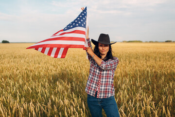 Woman farmer wearing cowboy hat waving american usa flag at wheat field.