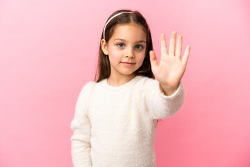Little caucasian girl isolated on pink background saluting with hand with happy expression