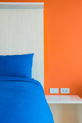 A part of modern and minimalist interior of bedroom. Blue bed with orange wall.