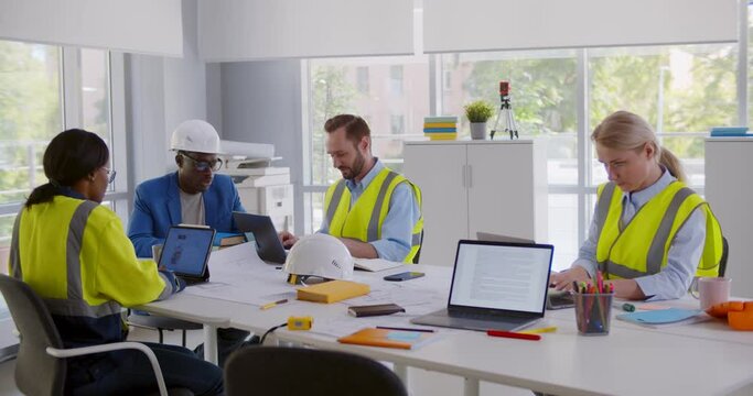 Afro-american businessman in helmet giving presentation engineering team sitting in office