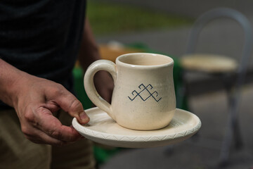 A white clay mug and a plate in the man's hand.
