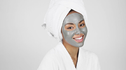 African american woman with clay mask on face and towel on head smiling isolated on grey