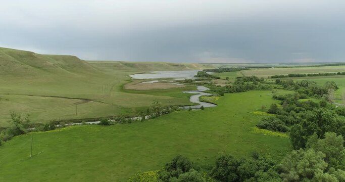 Source of the river with beauty calm swampy backwater with reeds and thickets and bald hills background. Aerial above drone wide view at summer cloudy day.