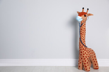 Toy giraffe with face mask and stethoscope near white wall, space for text. Pediatrician practice © New Africa