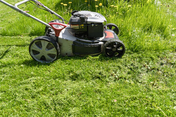 Fototapeta na wymiar Gasoline lawn mower while working on mowing a spring lawn from the side