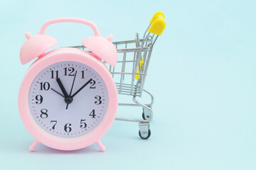 Shopping time. Shopping cart and pink alarm clock on blue background. Copy space for text.	