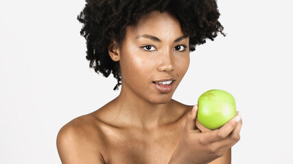 Pretty african american woman with clean face holding green apple isolated on grey