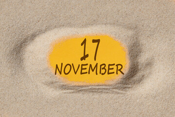 November 17. 17th day of the month, calendar date. Hole in sand. Yellow background is visible...