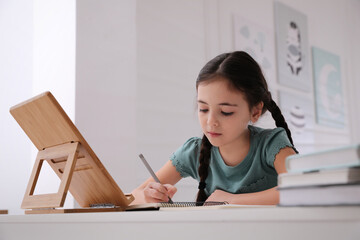 Little girl doing homework with tablet at table in room