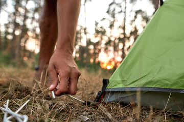 Close up shot of male hand setting up camping tent in forest at sunset
