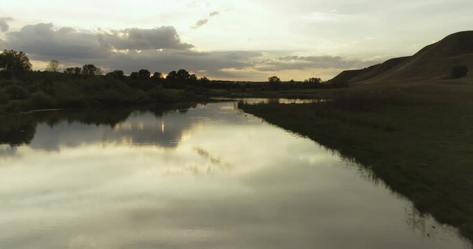 Source of the river with beauty calm swampy backwater with reeds and thickets and bald hills background. Aerial above drone wide view at summer evening sky.