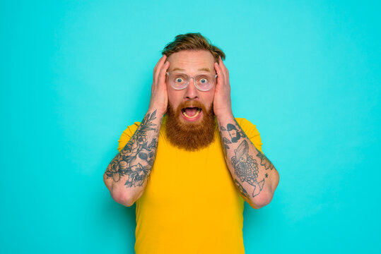 Man with yellow t-shirt and beard is shocked about something