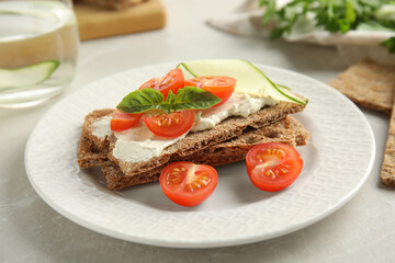 Fresh rye crispbreads with cream cheese and vegetables on light grey table, closeup
