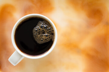 Top view of black coffee cup with bubbles on top, placed on the floor that  mix of brown, white. It's looks like coffee with milk or like marble.