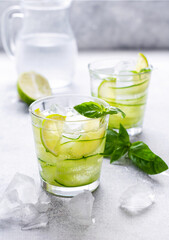 Refreshing summer homemade lemonade made from lime, lemon, cucumber and basil with ice in glass on old concrete background. Selective focus