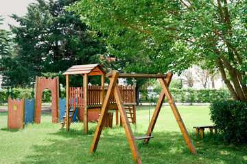 Wooden playground with swings on a green lawn among the trees