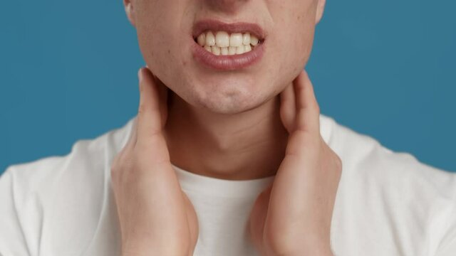 Inflamed glands. Unrecognizable man massaging his painful neck, suffering frome cold or flu, blue studio background