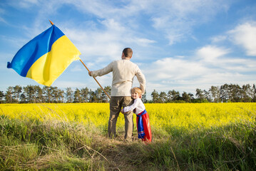 dad and son, stand side by side in national Ukrainian clothes with large yellow - blue flag of...