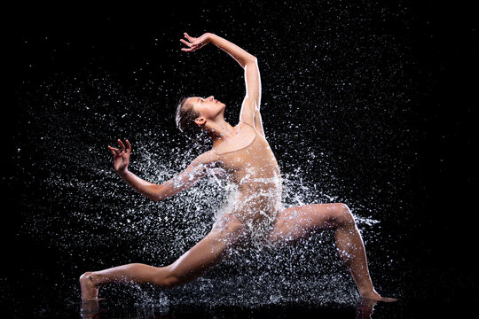 Wet young woman in tight beige swimsuit is dancing on floor under rain and splashes, drops of water. Girl modern dancer is doing tricks. Contemporary art dance. Freedom and freshness concept.