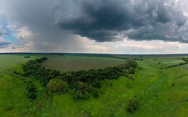 Fototapeta na wymiar Aerial panorama summer view, fly above green fields with stormy cloudscape. Dark rainy scenic heavy weather in rural agriculture area. Drone view