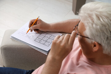 Senior man solving sudoku puzzle on sofa at home