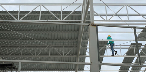 Worker climbing on steel structure to thatch the roof of building in the construction site.