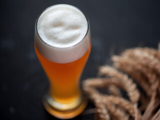 Top view of a glass of wheat beer close-up, black stone table, wheat ears
