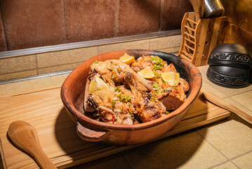Homemade grilled chicken with spices cut into pieces in red ceramic baking dish on wooden board.