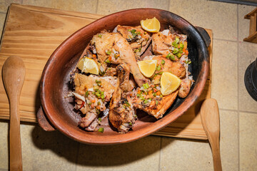 Homemade grilled chicken with spices cut into pieces in red ceramic baking dish on wooden board.