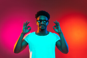 Portrait of young african man at studio on bright pink neon background. Concept of emotions and facial expression.