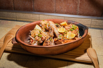 Homemade grilled chicken with spices cut into pieces in red ceramic baking dish on wooden board.