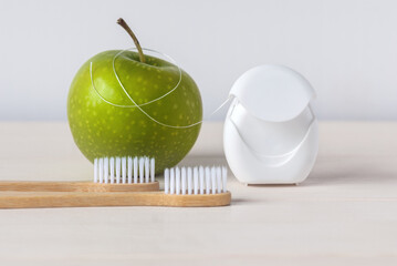 Bamboo toothbrushes, green apple and dental floss on white background - dental care routine to keep...
