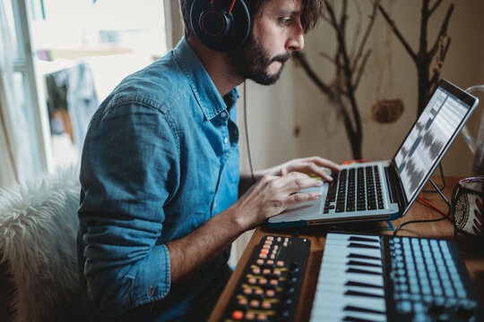 Musician using synthesizer and laptop at home