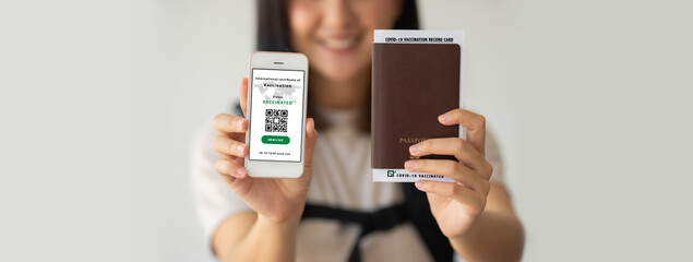 Selective focus, Asian female holding health passport of vaccination certification on smartphone and passport with vaccination label inside at the airport. Travel concept during COVID-19 pandemic.
